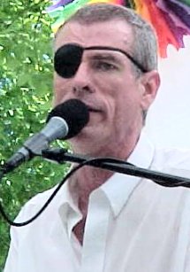 PHOTO: A close-up of Steve singing in Davis California -- wearing a black eyepatch on his right eye. Gaze slightly downcast. Singing Will It Always Be Like This?