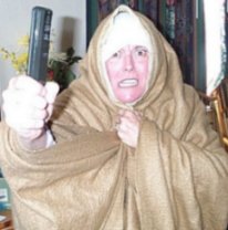 Picture: Linda D. is wearing a nun outfit made of a brown bed spread over a sheet made to lookin like a wimple. She is holding a TV remote in her hand like a ruler. She is grimacing madly.