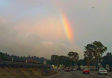 Pictured is a bright, colorful rainbow stretching from the gray sky down to the Hollywood Hills.
