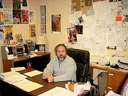 Chris Kawolsky seated at a desk dwarfed by the walls of a theatrical producer. Papers tacked to other papers. But somehow all neat.